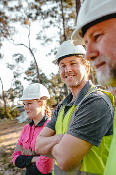 Three construction workers standing on worksite with arms crossed.