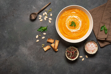 Pumpkin cream soup in a bowl with croutons, spices and seeds on dark grunge background, top view, flat lay. Warming Winter and Autumn Soup. Vegan Soup