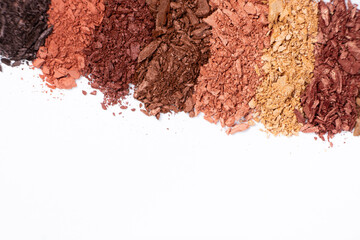 Scattered eye shadows in different shades. Cosmetics texture, white background.