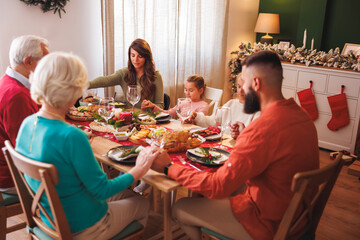 Family holding hands praying with eyes closed before Christmas dinner at home