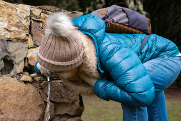 Mature woman hiking in national park quenches thirst at drinking fountain. Leisure activity in...