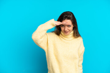 Young caucasian woman isolated on blue background looking far away with hand to look something