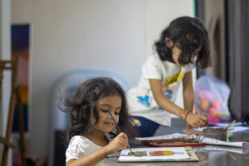 Two sisters are doing art work with water color on paper at home.
