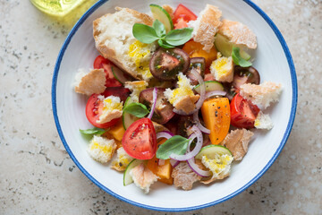 Blue and white plate with tuscan-style tomato and bread salad or panzanella, horizontal shot on a beige granite surface, middle closeup