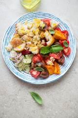 Blue and white plate with italian panzanella salad, vertical shot on a beige stone background, high angle view