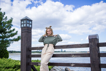 Fototapeta premium young blond woman in a sweater and trousers stands on a bridge on the lake, smiles, poses, photosession
