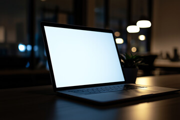 A blank white screen of an open laptop placed on the table in front view with a blurred background, a concept for displaying images or text. The scene is set against a blurry office interior backdrop.