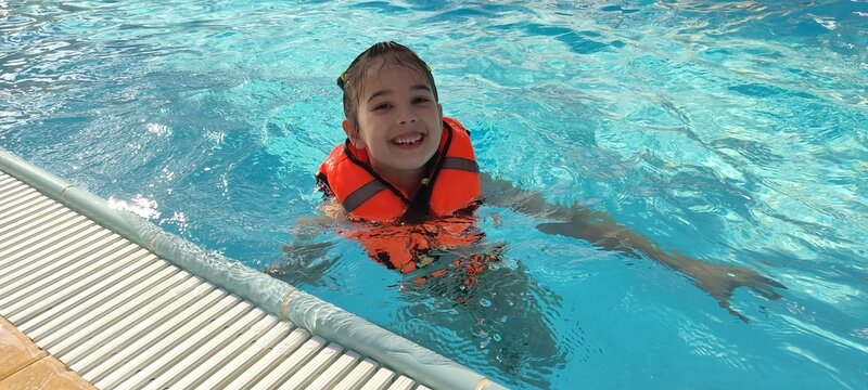 Happy child in orange life jacket enjoying a swim in clear blue pool