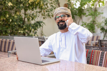 Happy Omani man on call through mobile phone at a coffee shop