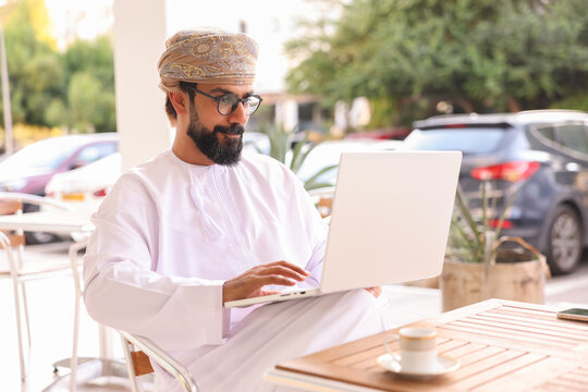 Cheerful omani man sending a mail on laptop