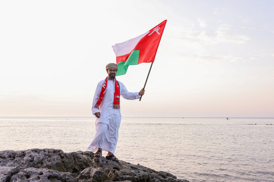 Omani man holding omani flag with one hand at the beach
