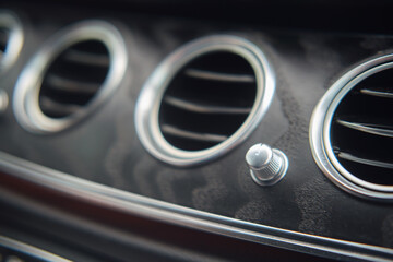 Close-up of car air vents and a control knob on a black dashboard. Macro shot of vehicle interior details. Automotive design and control concept.