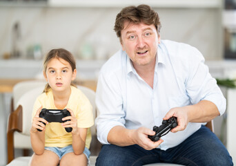 Family, gaming and entertainment concept - happy father and little daughter with gamepads playing video game