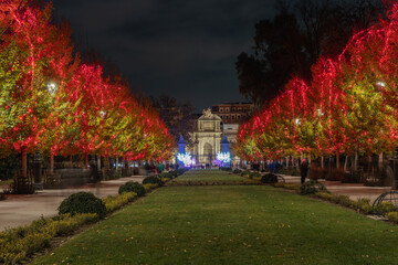 Christmas night in the Paseo De Méjico of th El Parque del Retiro with red lights in the trees and in the background the Puerta de Alcalá