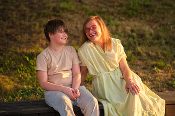 An affectionate portrait of a woman and her teenage son, both smiling with happiness against a lush green backdrop. A mature woman and her child boy enjoying a carefree day outdoors