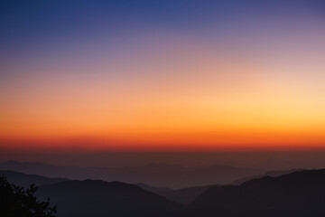 The sky gradient from blue to orange over the mountains. The mountains look like an oriental painting.