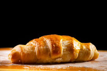 A fresh croissant with a golden, crispy crust and flaky texture lies on a wooden board. Organic baking