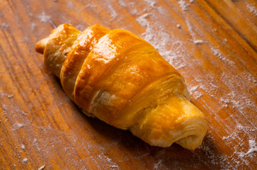 A fresh croissant with a golden, crispy crust and flaky texture lies on a wooden board. Organic...