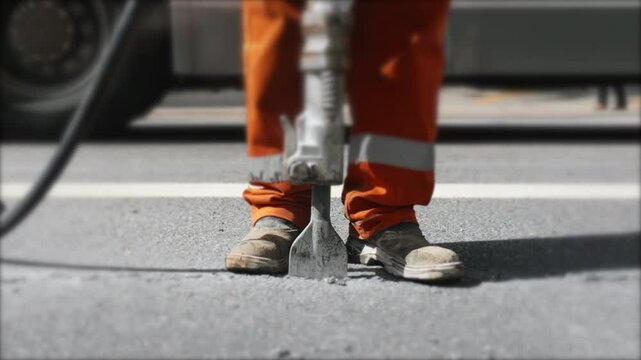 Worker operating a jackhammer on a city street, breaking asphalt during a construction job, wearing protective gear and showcasing the intensity of manual labor