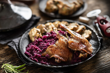 Portion of roast duck leg red cabbage homemade dumplings on plate and red wine on the background