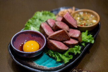 Grilled beef tongue served on plate with pickled egg yolk and sauce