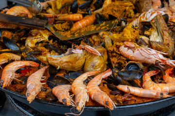 Street food in France, fresh prepared colorful paella with rice and sea food in big pan on street market ready to eat