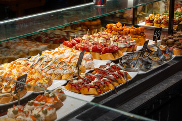Typical snacks of Basque Country, variety of pinchos or pinxtos oven baked sea food, bread, skewers with jamon, goat cheese served in bar in San-Sebastian or Bilbao, Spain, close up