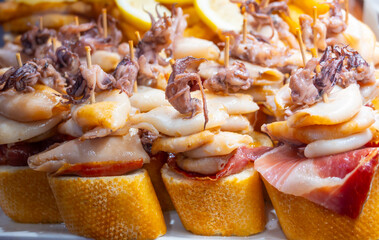 Typical snacks of Basque Country, pinchos or pinxtos skewers with small pieces of bread, fish, sea food, sweet green pepper served in bar in San-Sebastian or Bilbao, Spain