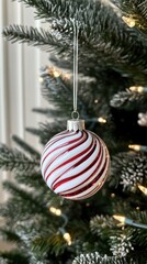 A vibrant red candy ornament hangs delicately from a snow-covered Christmas tree adorned with twinkling lights during the holiday season