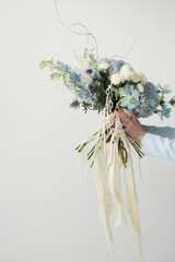 Elegant hand-held bouquet featuring blue and white flowers against a neutral background in bright natural light