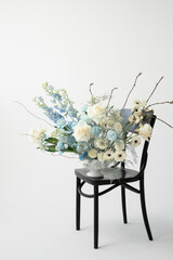 Elegant floral arrangement in soft blue and white colors displayed on a black wooden chair against a minimalist background