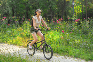 Obraz premium Asian girl with long hair rides old bicycle on city park paths
