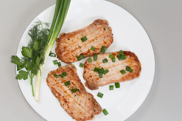 Grilled boneless pork chops with greens on dish, top view