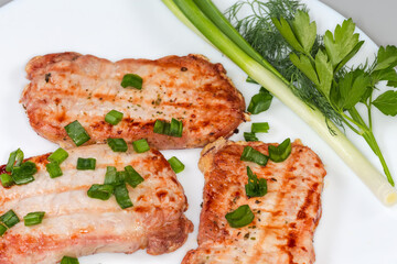 Grilled boneless pork chops with greens on dish, close-up