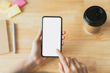 Top view of hand holding black smartphone with blank screen on wood background.