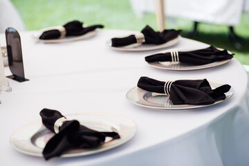 Outdoor wedding banquet. The tables are covered with tablecloths. There are various accessories and plates with napkins on the tables.