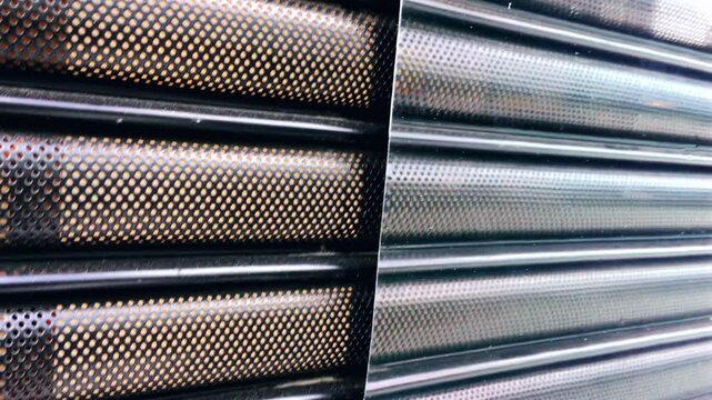 Metal gate of a business store being raised upwards, close-up view of the perforated metal pattern as the gate opens, revealing the storefront during opening hours