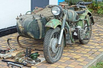 one old green iron retro dirty powerful heavy with sidecar historical military army broken with glass electric headlight and wheels stands  on concrete road near white wall daytime outdoors