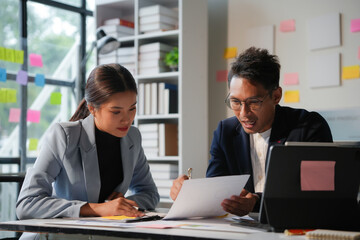 Two young professionals are working together, reviewing documents and talking in their office
