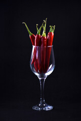Hot red chili peppers in a wine glass. Still life on a black background. Bright pepper.