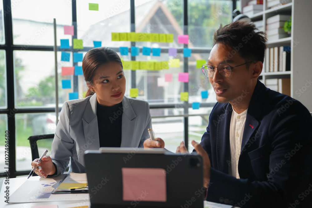 Wall mural two business people having a meeting discussing a new project using sticky notes on a glass wall in 