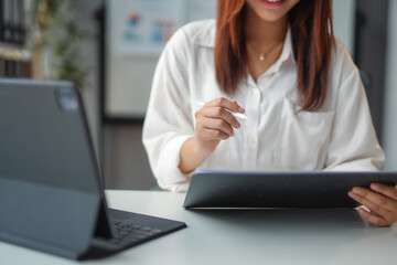 Businesswoman is holding a stylus and working on a tablet with another tablet lying on the desk