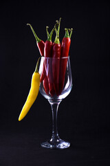 Hot red chili peppers in a wine glass. Still life on a black background. Bright pepper.