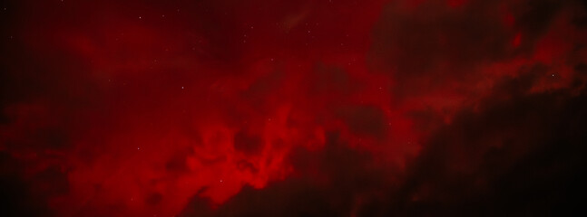 A dramatic view of the Aurora Borealis with intense red hues glowing through a cloudy night sky. The vibrant red contrasts with the dark clouds, creating a fiery and mysterious atmosphere.