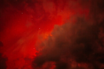 A dramatic view of the Aurora Borealis with intense red hues glowing through a cloudy night sky. The vibrant red contrasts with the dark clouds, creating a fiery and mysterious atmosphere.