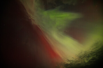 A striking display of the Aurora Borealis fills the night sky with vibrant green and red hues, radiating across the darkness. The lights blend together, creating a dynamic and ethereal effect