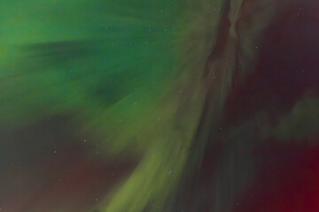 Fototapeta premium A striking display of the Aurora Borealis fills the night sky with vibrant green and red hues, radiating across the darkness. The lights blend together, creating a dynamic and ethereal effect