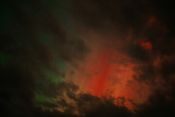 Fototapeta premium A captivating scene of the Aurora Borealis with vibrant red and orange hues illuminating the night sky. Dark clouds add drama, while subtle green light emerges through the atmosphere