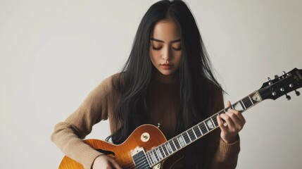 Fototapeta premium Musician practicing guitar, young Asian woman with long black hair, modern studio, copy space