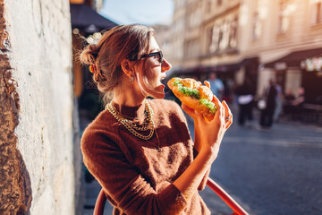 Young woman having fresh croissant in outdoor cafe at sunset. Customer enjoys street food in Lviv eating bakery